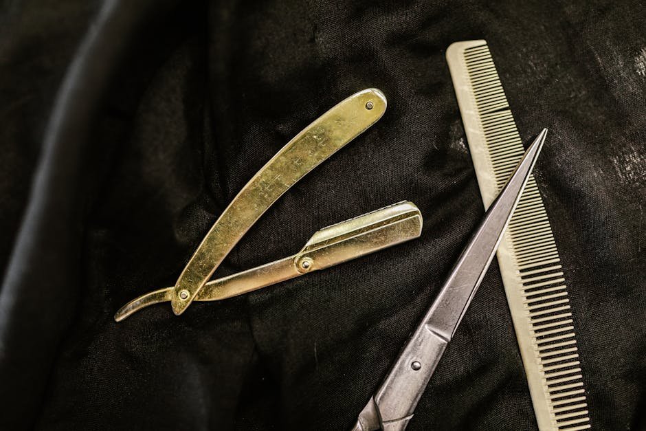 Close-up of silver shears, comb, and straight razor on a black cloth background, highlighting barber tools.